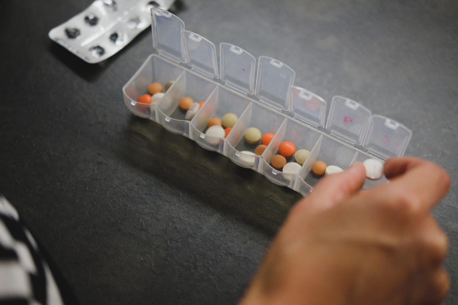 A hand beside a medicine organizer; illustrative medication-management photograph, not identification of a specific medicine.