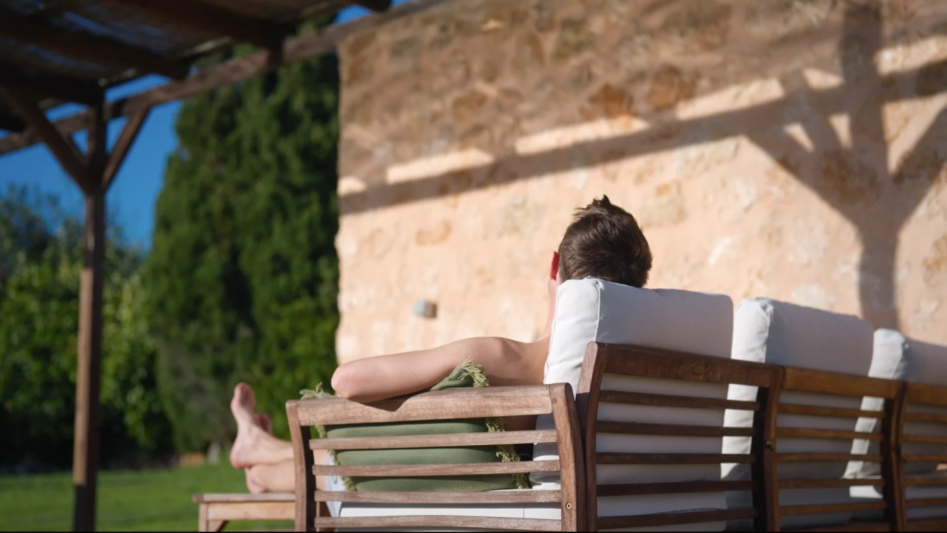 Person resting on an outdoor lounge sofa beside a stone wall