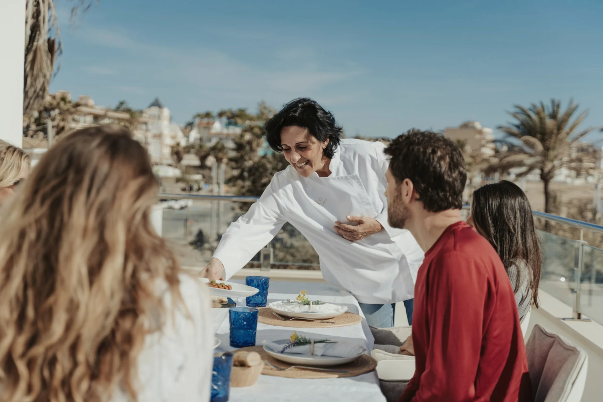 Chef serving food to people seated at an outdoor table